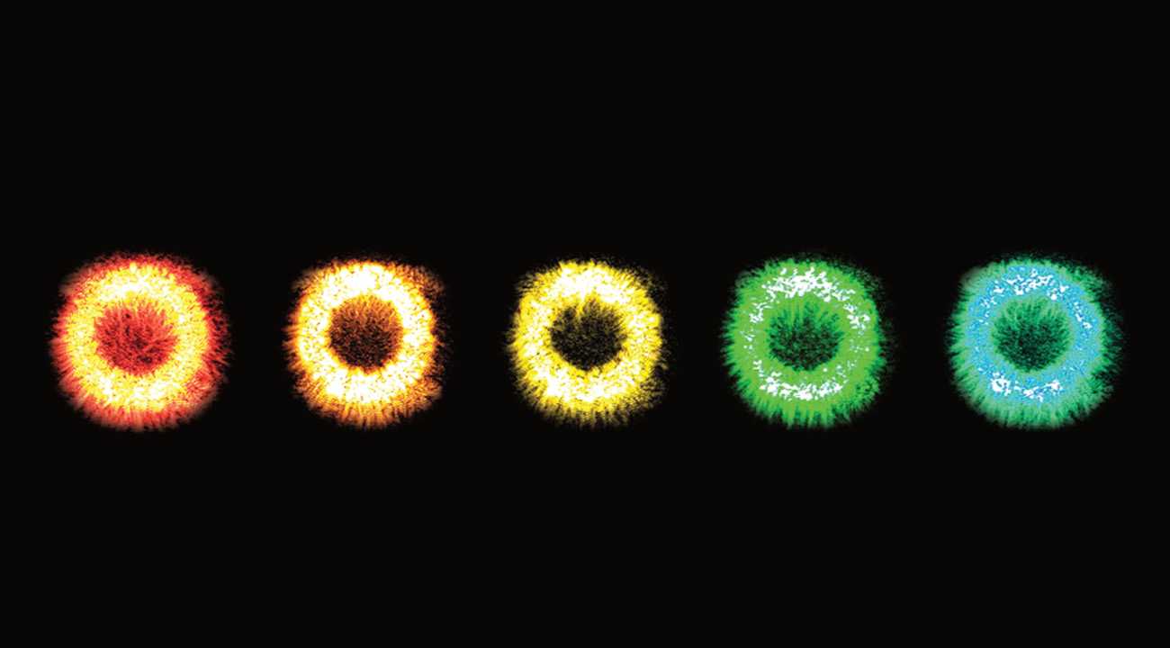 Five glowing rings with flame like filaments in a row against a black background. From left to right they are reddish-orange, orange, yellow, green and a greenish-blue. 